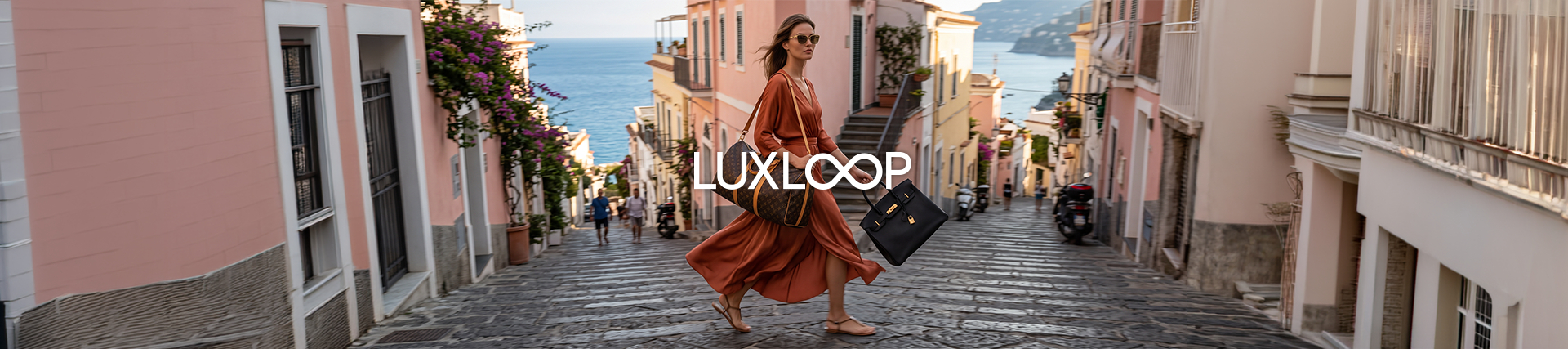 Frau in rostfarbenem Kleid trägt zwei Designer-Handtaschen auf einer mediterranen Straße mit Blick auf das Meer.